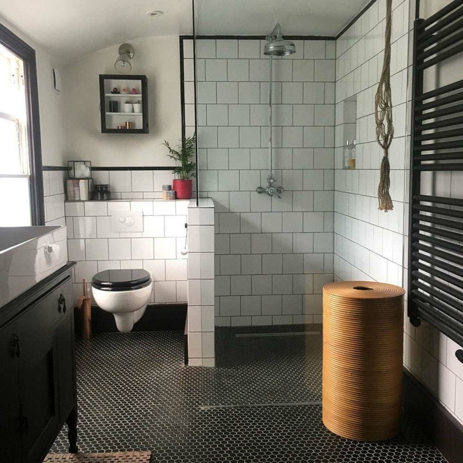 A natural tan woven wicker laundry basket with a cylindrical shape shown against a black honeycomb floor mosaic