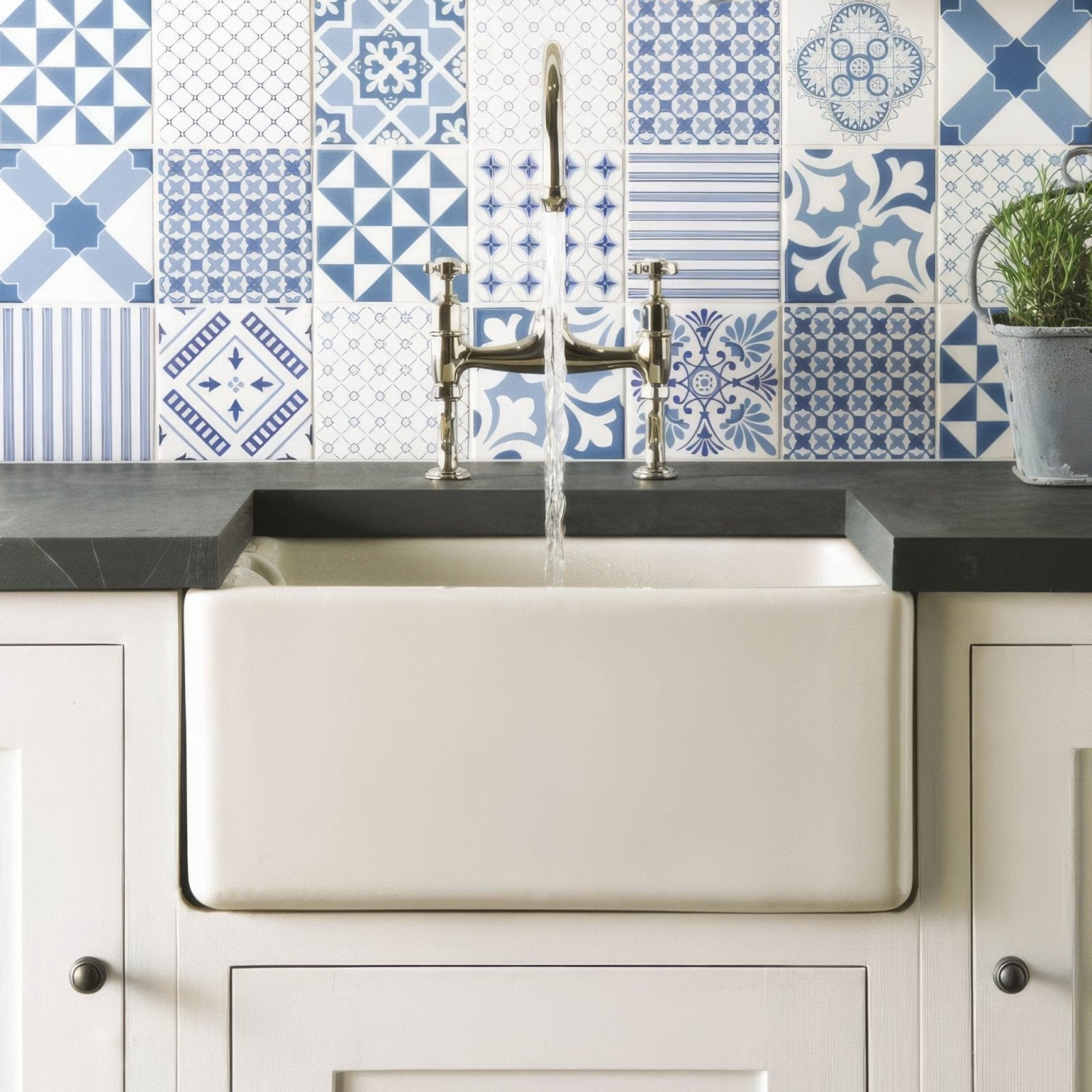 Cream-colored farmhouse sink with polished brass faucet against blue and white patterned tiles in blue tapestry set 12 on brilliant white