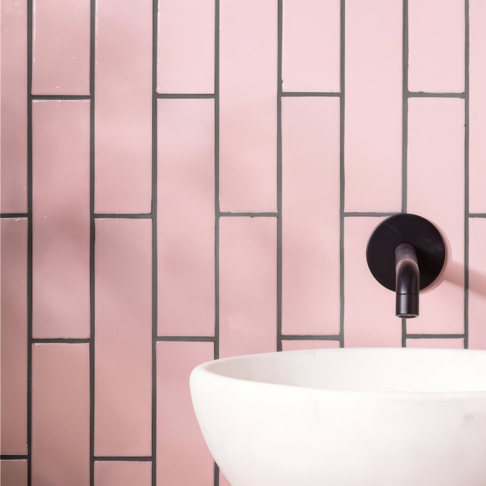 A sleek matte black wall-mounted faucet with minimalist design shown against blush smooth brick tile background