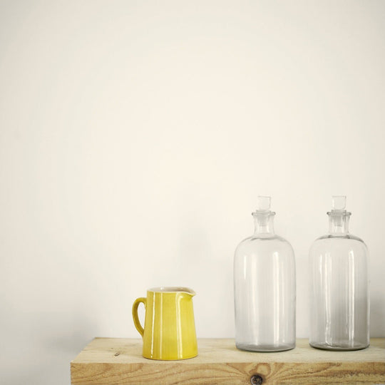 A vibrant yellow bone white ceramic pitcher with a smooth glossy finish and curved handle on a wooden surface