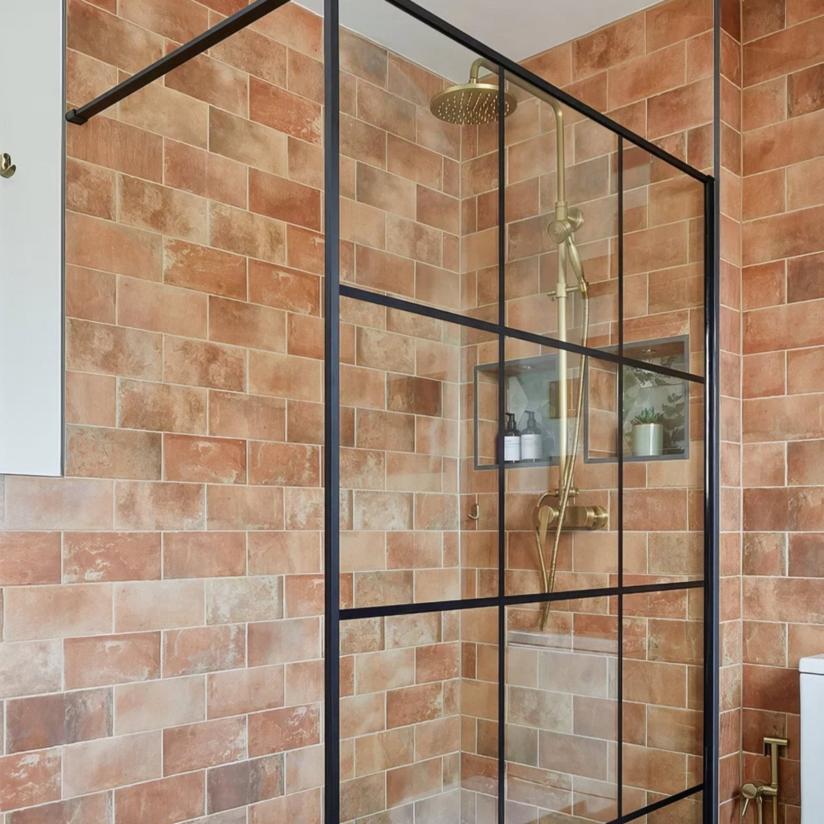 Modern black-framed glass shower enclosure with gold-toned rainfall showerhead in brewhouse porcelain brick setting