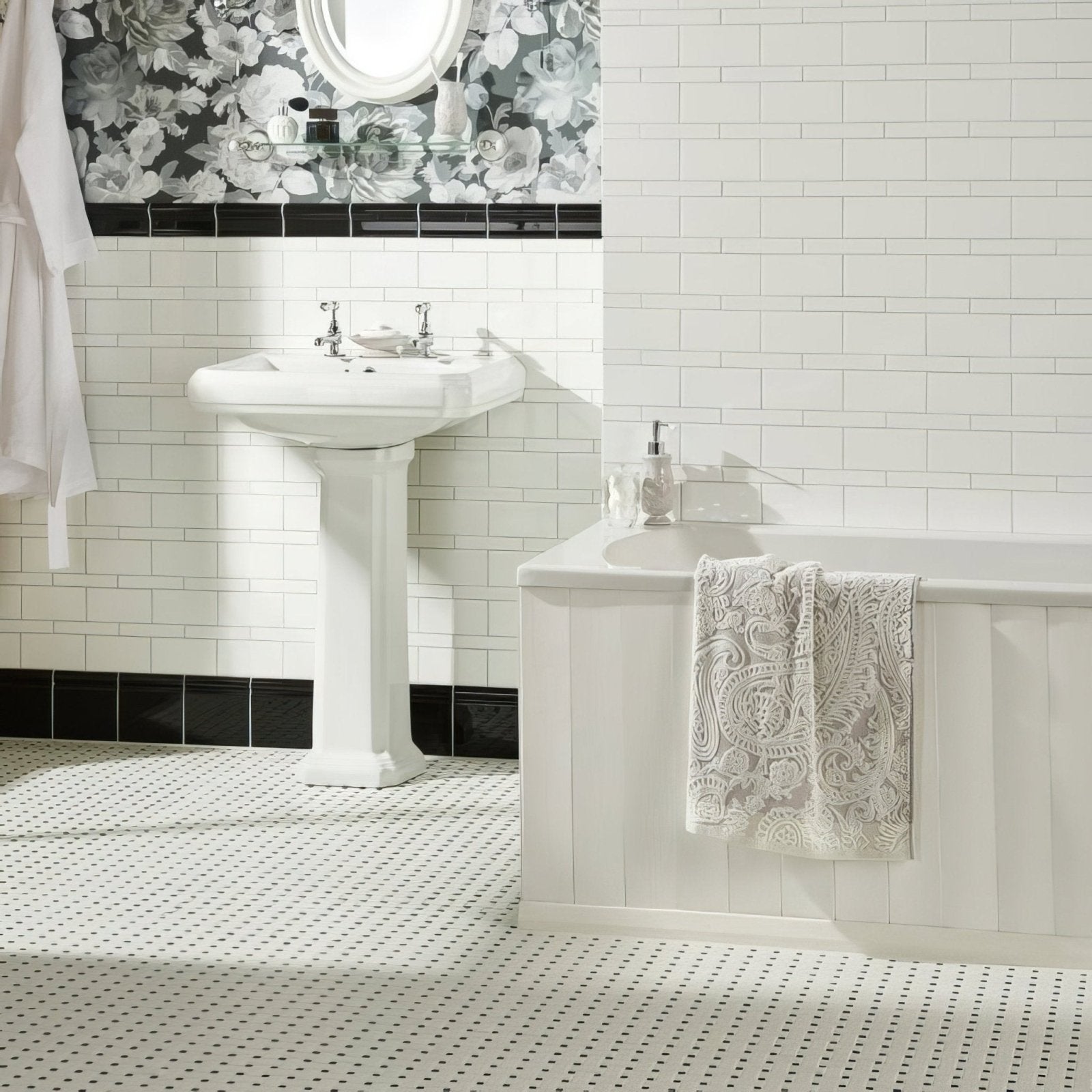 White pedestal sink with chrome faucets installed against brilliant white half tile wall in bathroom setting