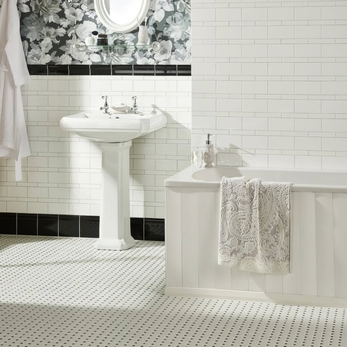 White pedestal sink with chrome faucets installed against brilliant white half tile wall in bathroom setting