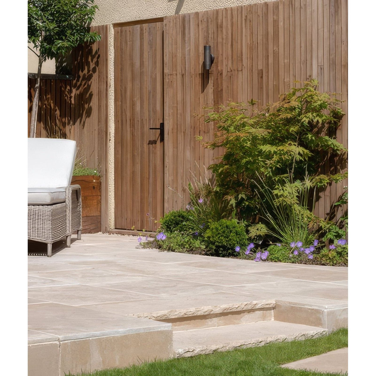 Beige buscot limestone paving with etched finish on a stone patio featuring integrated steps and a wooden fence backdrop