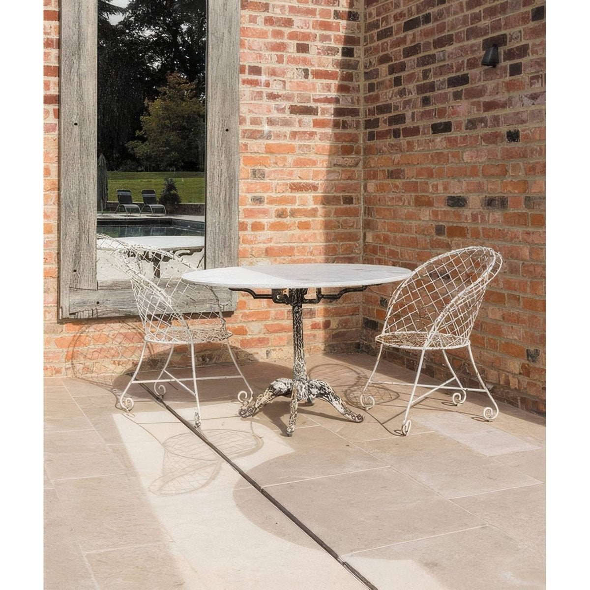 White wrought iron table with marble top and ornate scrolled legs featured with buscot limestone paving tumbled and etched finish