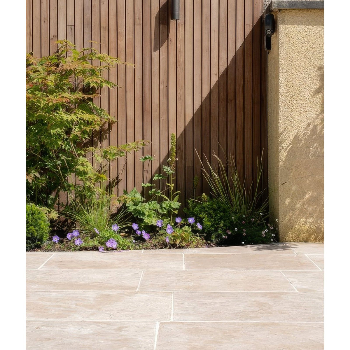 Brown vertical wooden fence beside beige textured stucco wall with Buscot limestone paving tumbled and etched finish