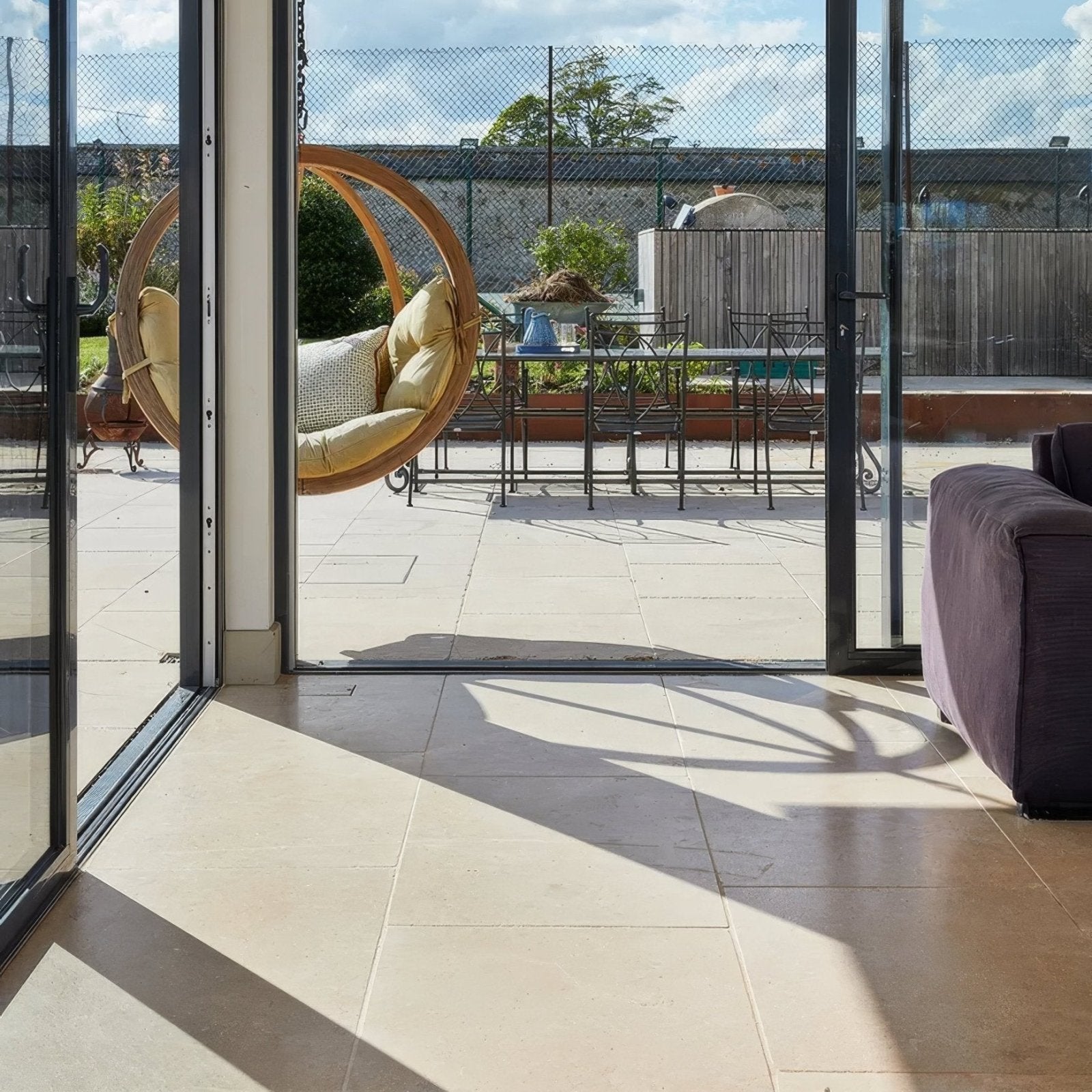 A hanging wooden swing chair with beige cushions and a woven circular frame in buscot limestone tumbled finish