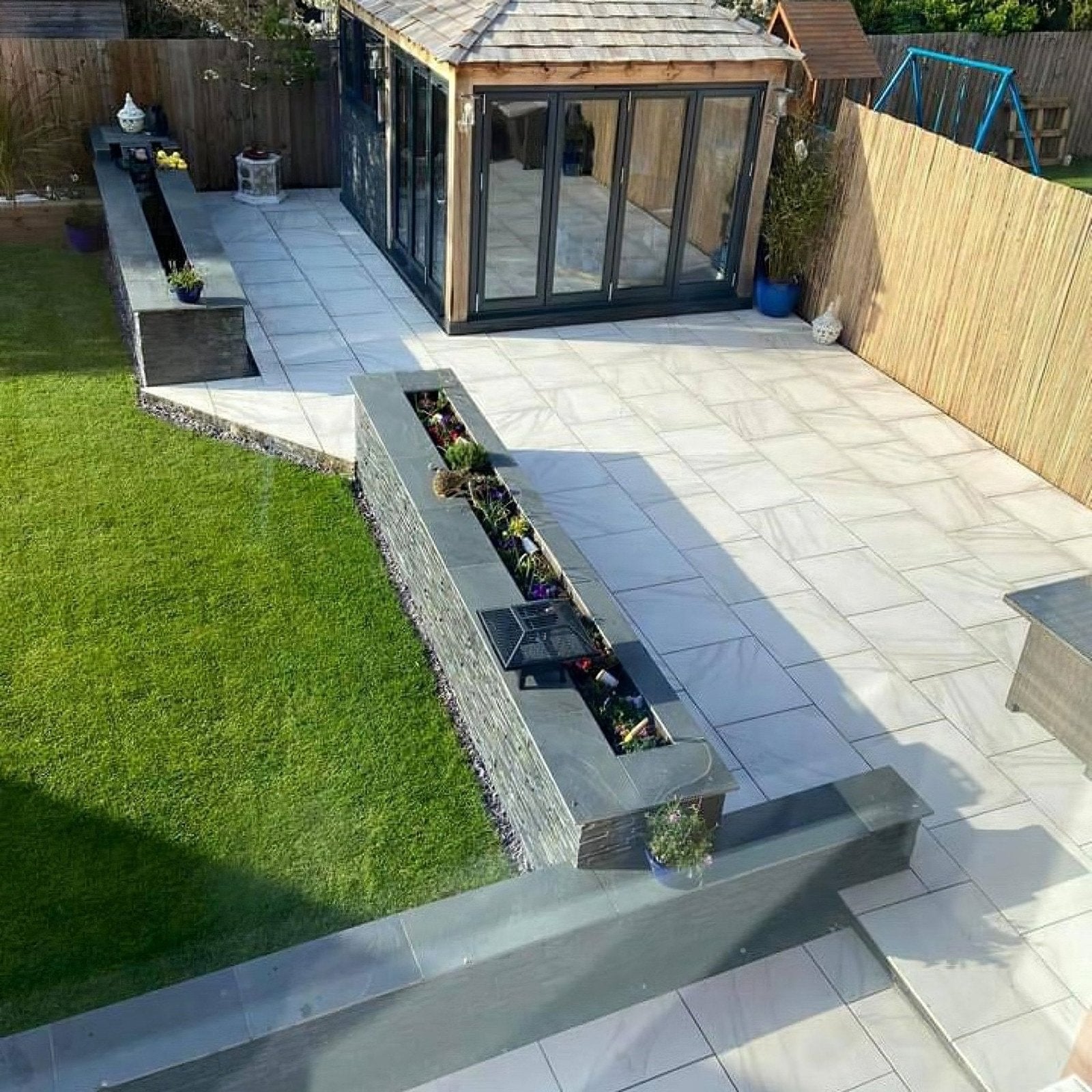 Modern gray calacatta gold matt porcelain paving on a stone patio with integrated planter box and glass garden room