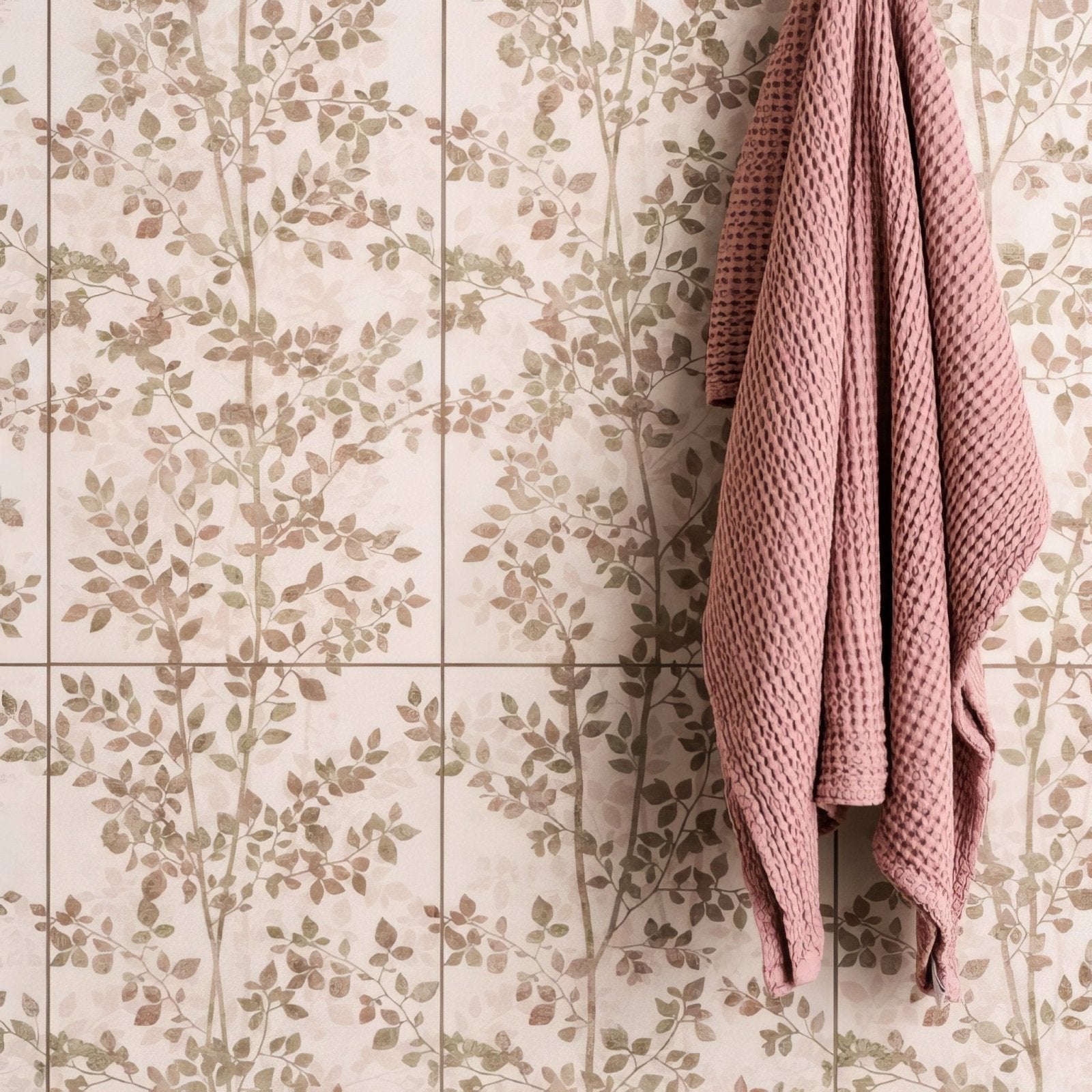 A soft pink waffle-weave canopy beech towel hanging against beige tiles with muted green and brown leaf patterns