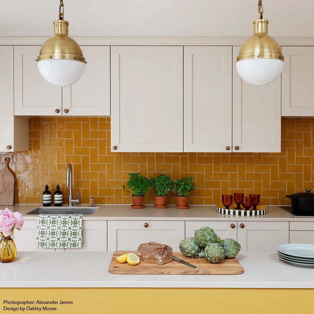 Gold-toned pendant lights with frosted glass shades hang above the kitchen counter near carnival oro yellow glazed tile