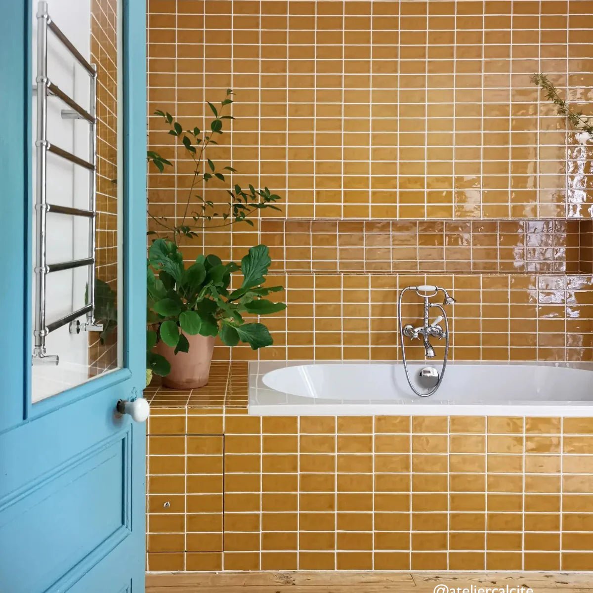 A white bathtub with a chrome faucet set against mustard yellow glossy carnival oro yellow glazed ceramic tiles