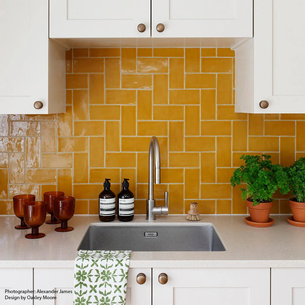 Vibrant mustard yellow carnival oro glazed tile with glossy finish in a herringbone backsplash design