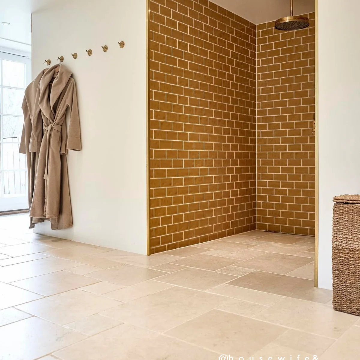 A beige robe with a tied waist hanging on a hook featured against carnival oro yellow glazed tile background