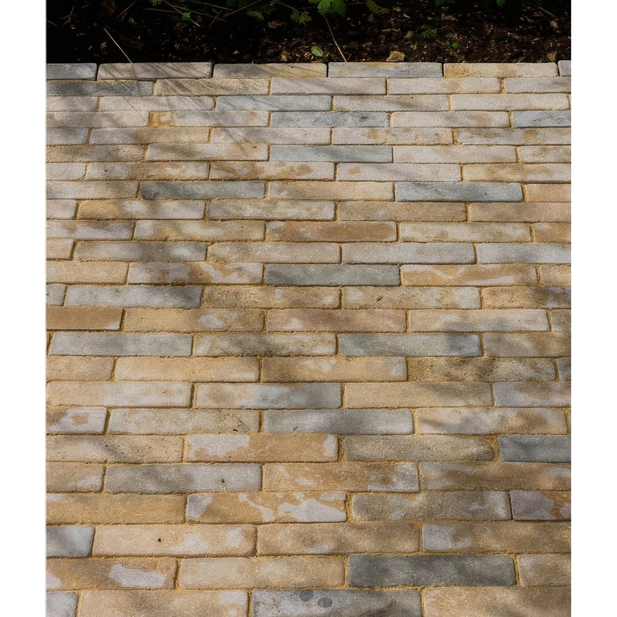 A paved walkway of castilan limestone tumbled klinkers with interlocking beige tan and gray rectangular pavers