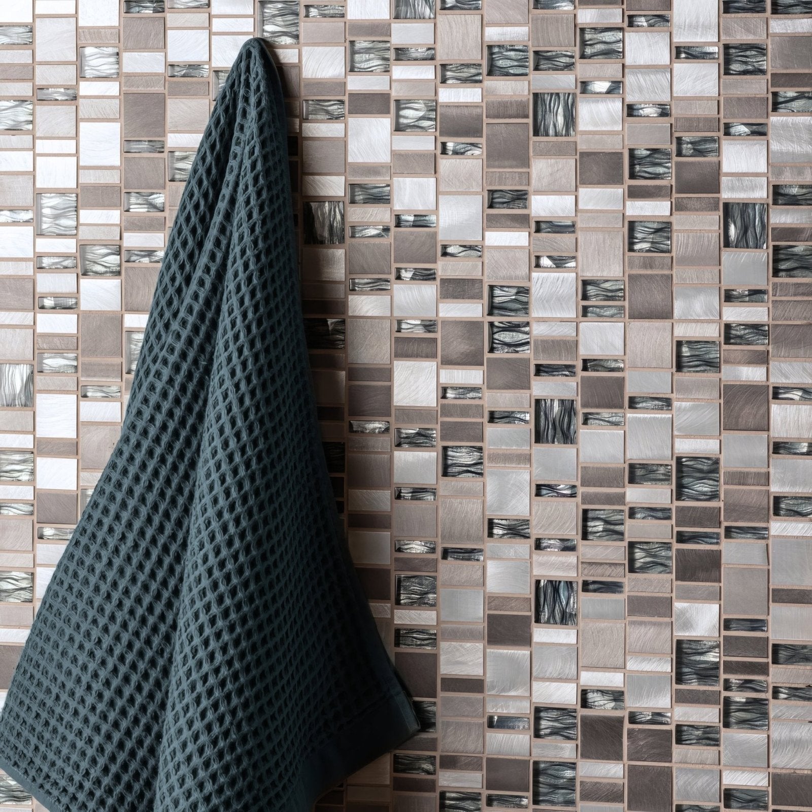 Dark teal waffle-weave towel hanging against a ceres rectangle mix mosaic tile wall background