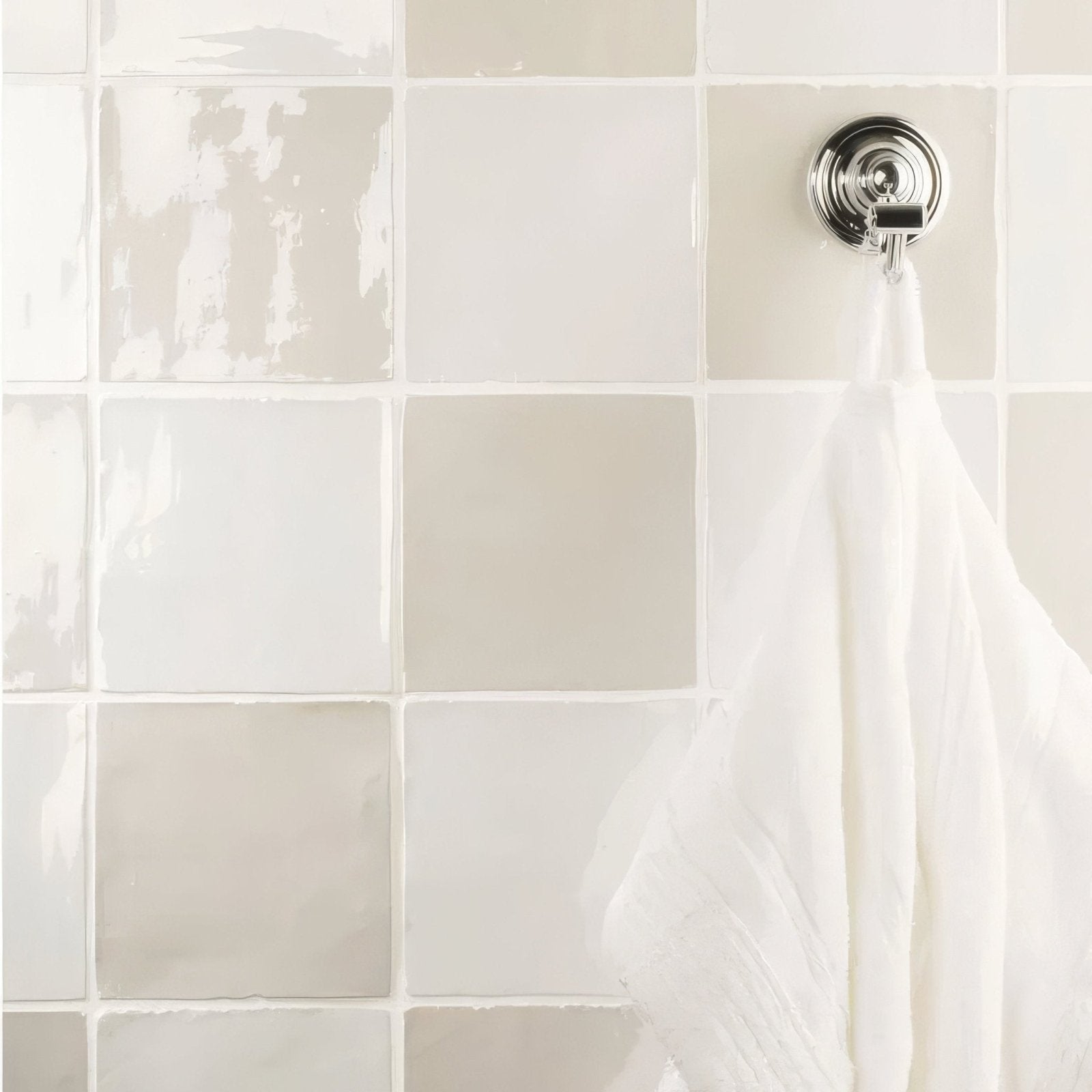 A white textured towel hanging on a chrome hook against light gray and off white chalk field tile background