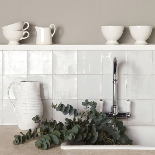 White ceramic pitcher with a textured handcrafted finish and curved handle on chalk field tile surface