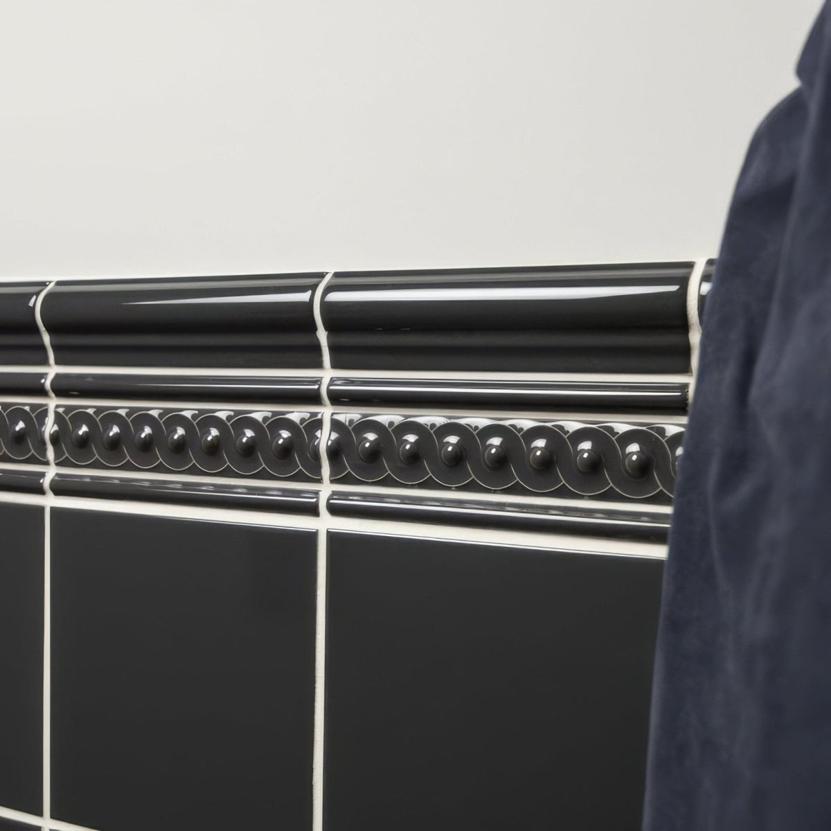 Charcoal Grey Omega Moulding running as a bead course in gloss ceramic above field tiling with white grout