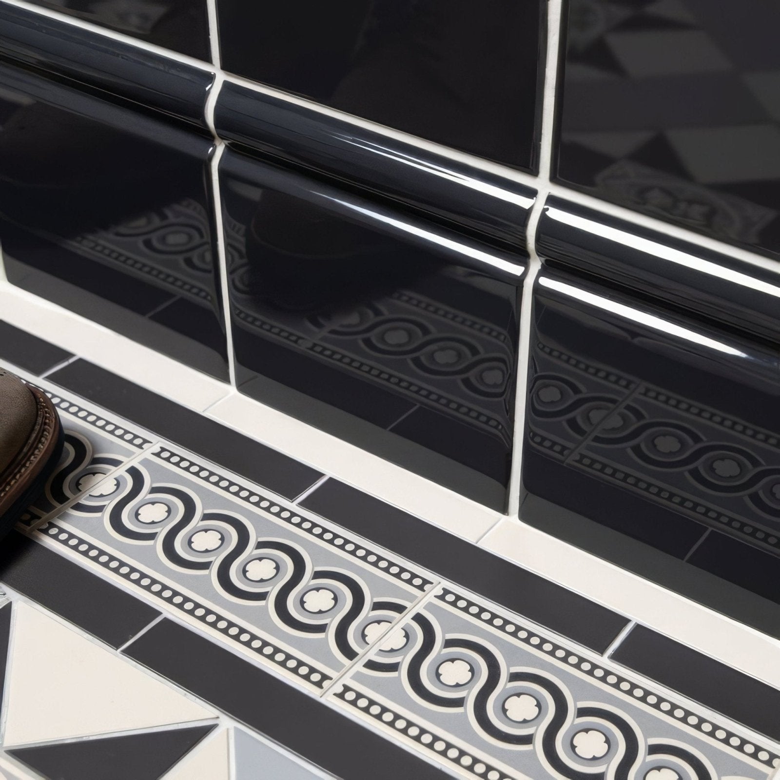 Charcoal grey skirting tile with black glossy ceramic surface white grout and intricate gray geometric patterns