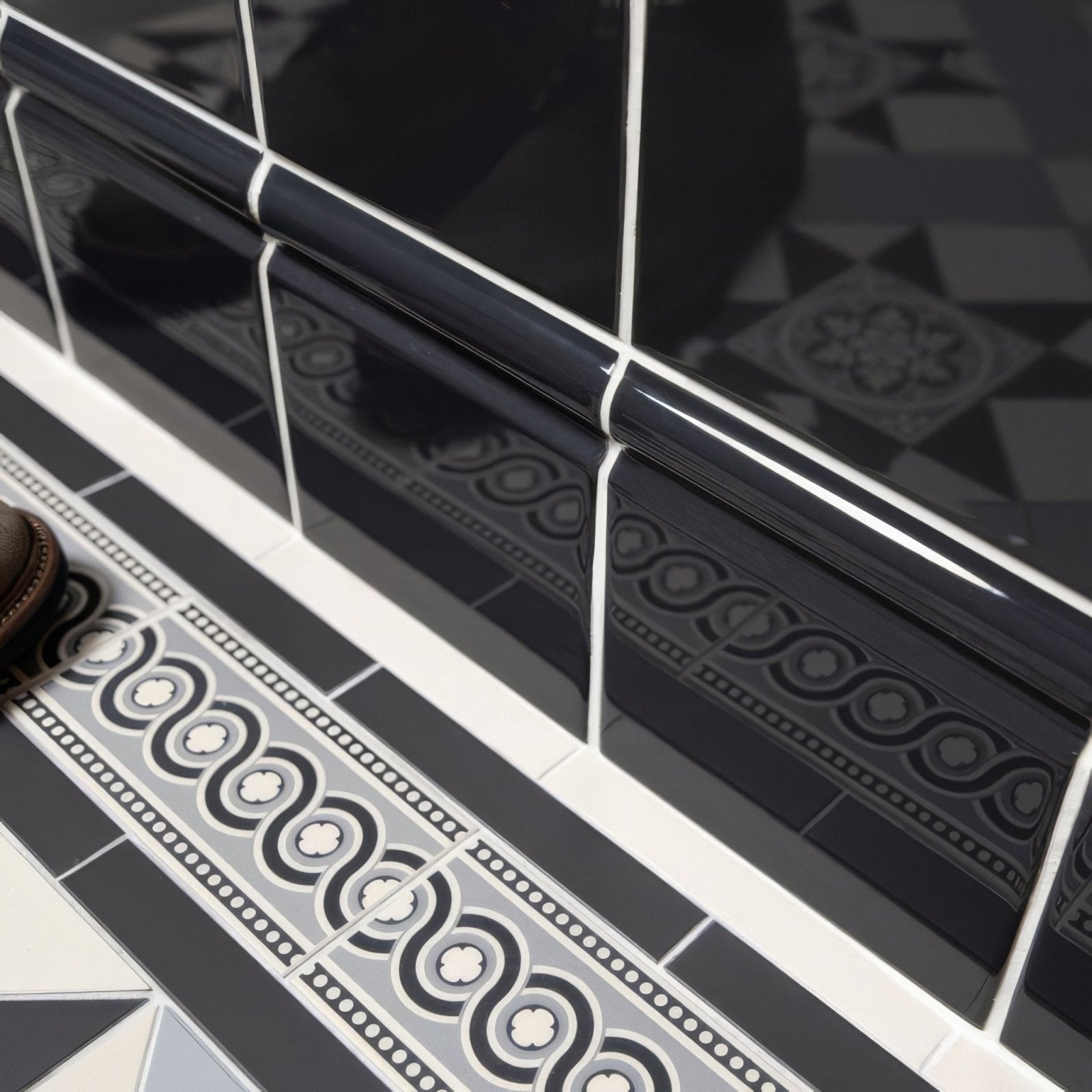 Charcoal grey skirting tile in black glossy ceramic with decorative wave pattern and white grout edging