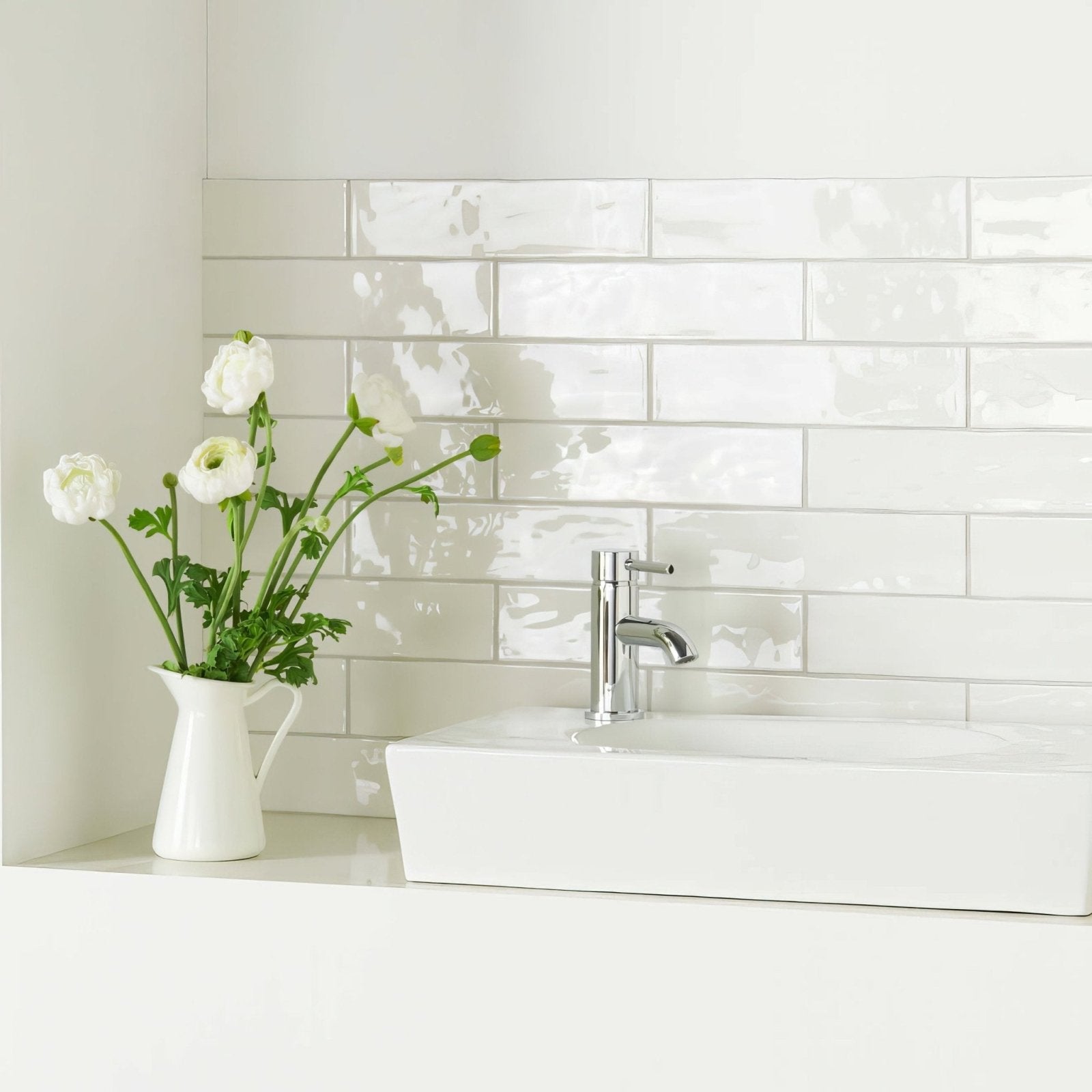 White ceramic pitcher holding white ranunculus flowers complementing china white large brick tile design