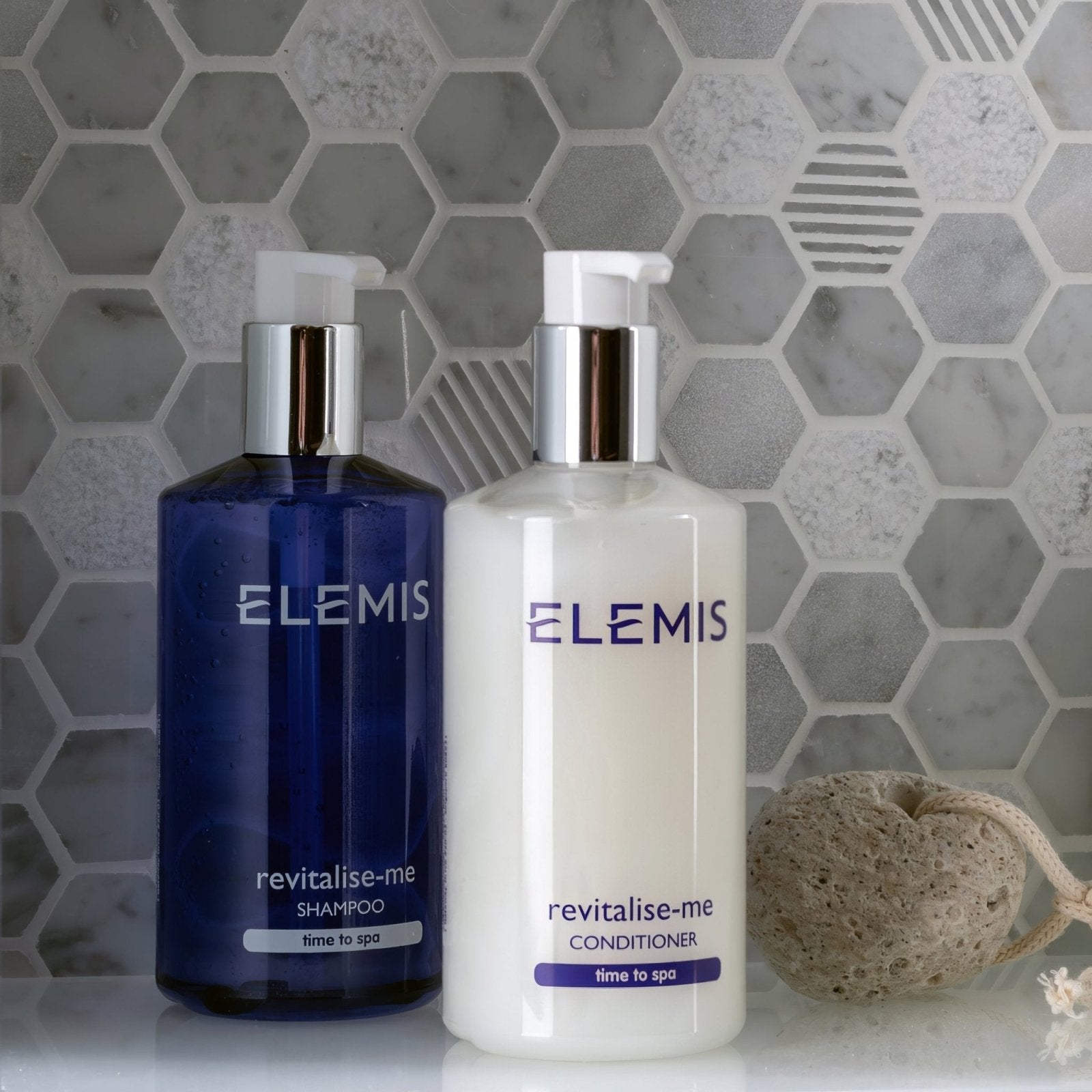 Blue and white elemis revitalise-me shampoo and conditioner bottles with silver pump tops on cirrus small stone hexagon surface