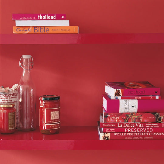 A tall clear glass bottle with a silver swing-top lid and slender neck on a red shelf labeled cochineal