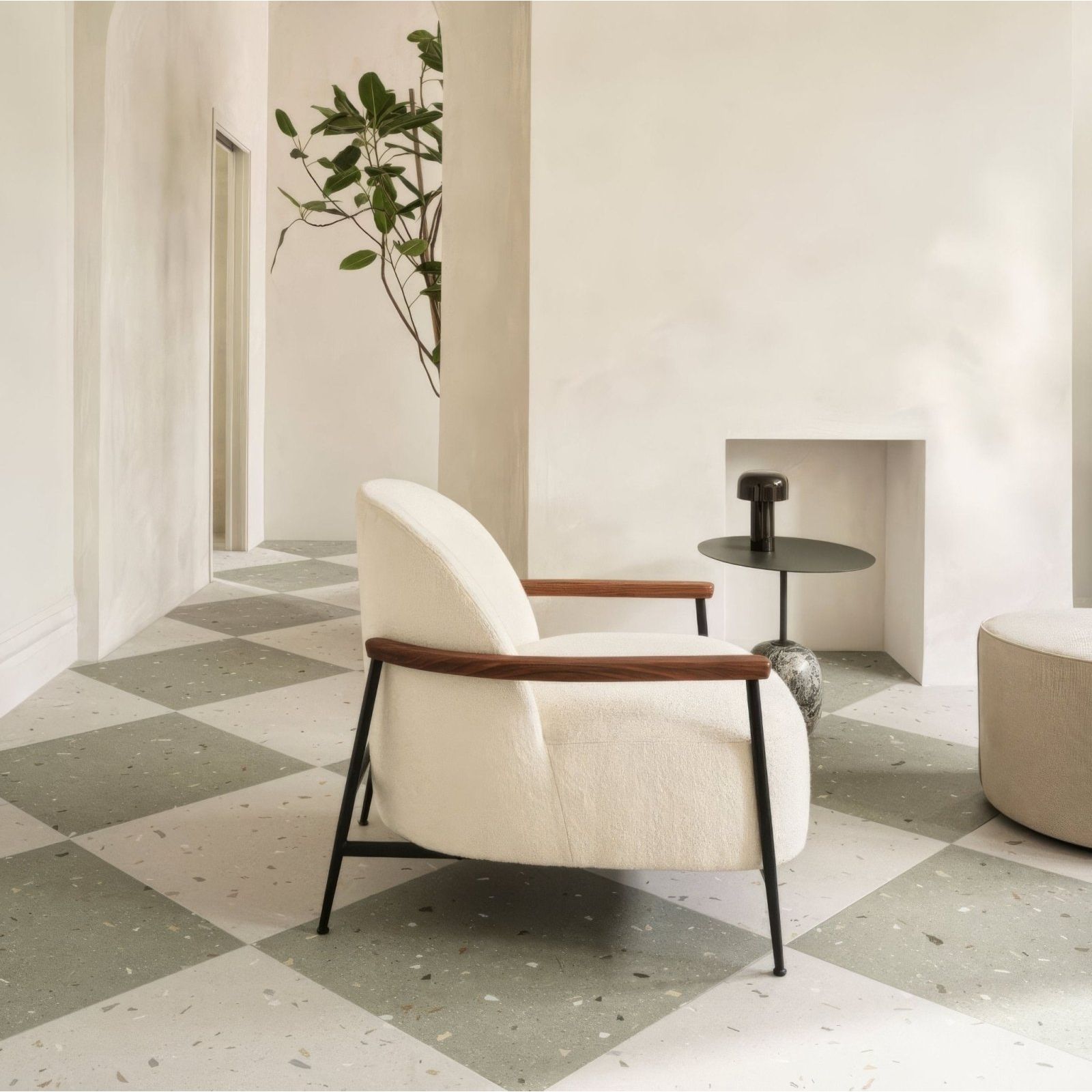 Cream-colored upholstered armchair with wooden arms and black metal legs paired with confetti cream terrazzo tile