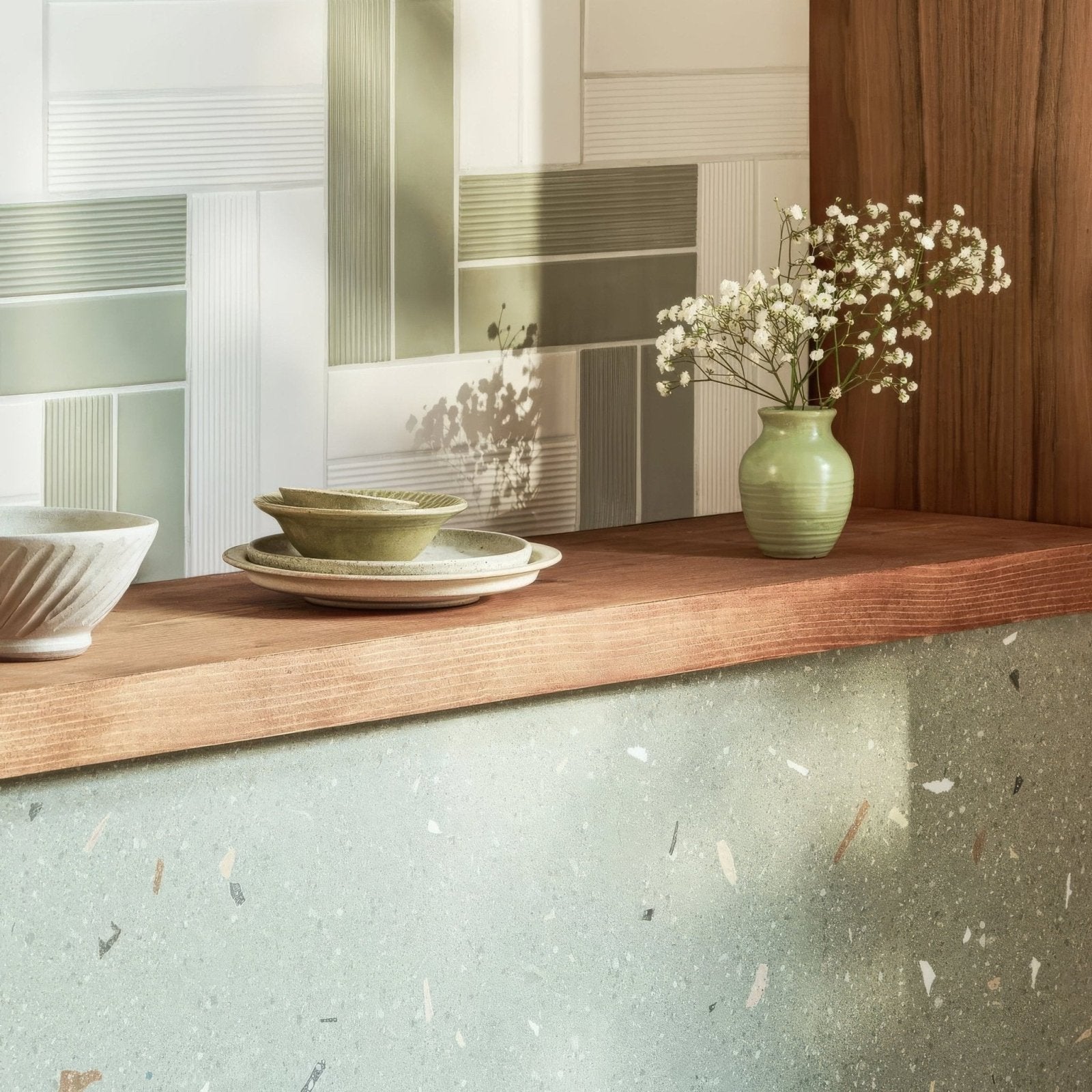 A sage green ceramic vase with subtle ridges holding white baby’s breath complements confetti green terrazzo effect tile
