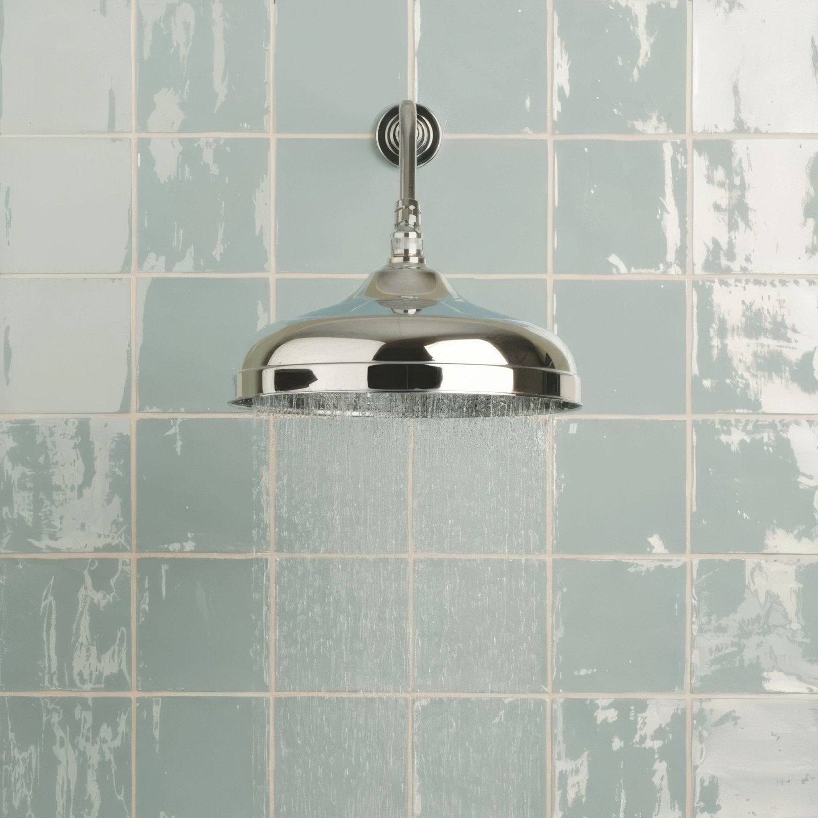 Shiny chrome showerhead with classic dome design mounted on a cornflower field tile wall