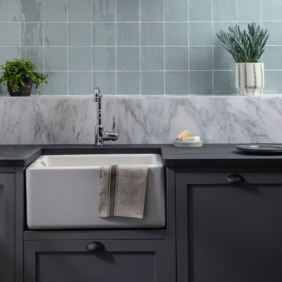 White ceramic farmhouse sink with towel draped over edge featuring blue cornflower field tile backsplash
