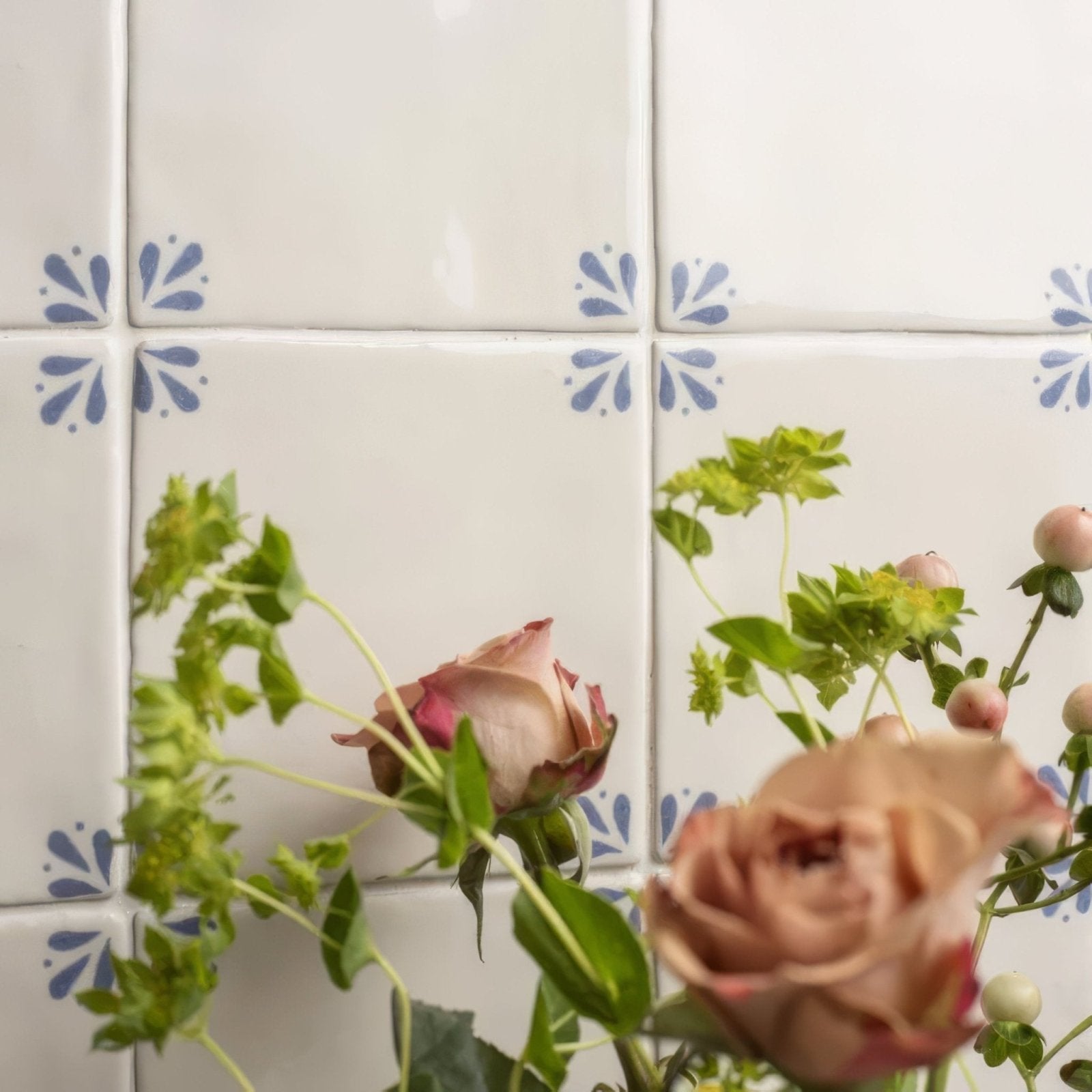 Country delft cornelia beige roses with green foliage in front of white ceramic tiles with blue floral patterns
