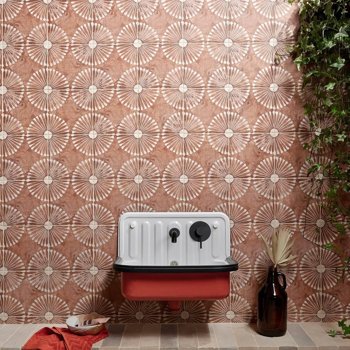 A vintage-style cuba porcelain vedado cotto enamel sink in white and red with black fixtures against a patterned wall