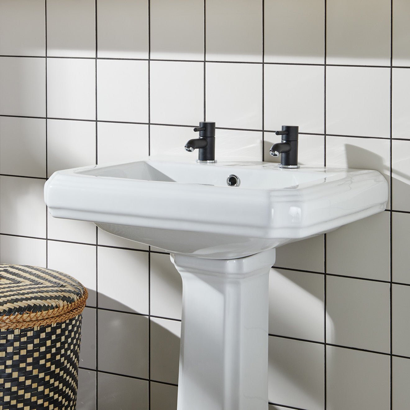 White ceramic pedestal sink with two black matte-finish faucets featured in daisy satin field tile setting