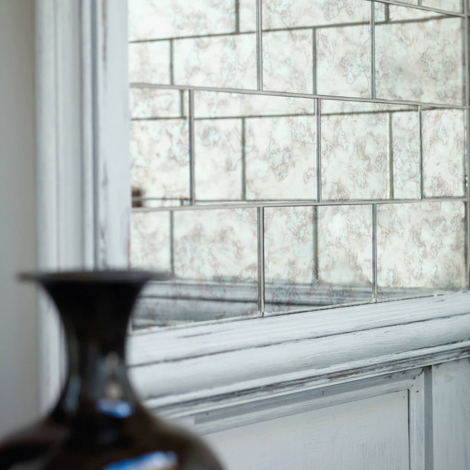 A dark glossy ceramic vase with a flared neck and rounded body featured with deco glass silver wall tile background