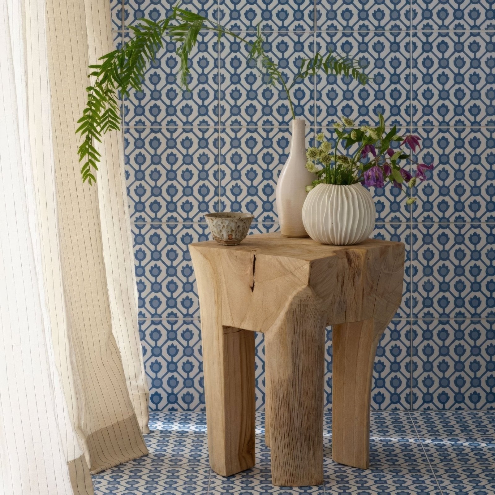 A rustic light-colored wooden side table with natural raw edge and sturdy legs by designers guild jaal cobalt