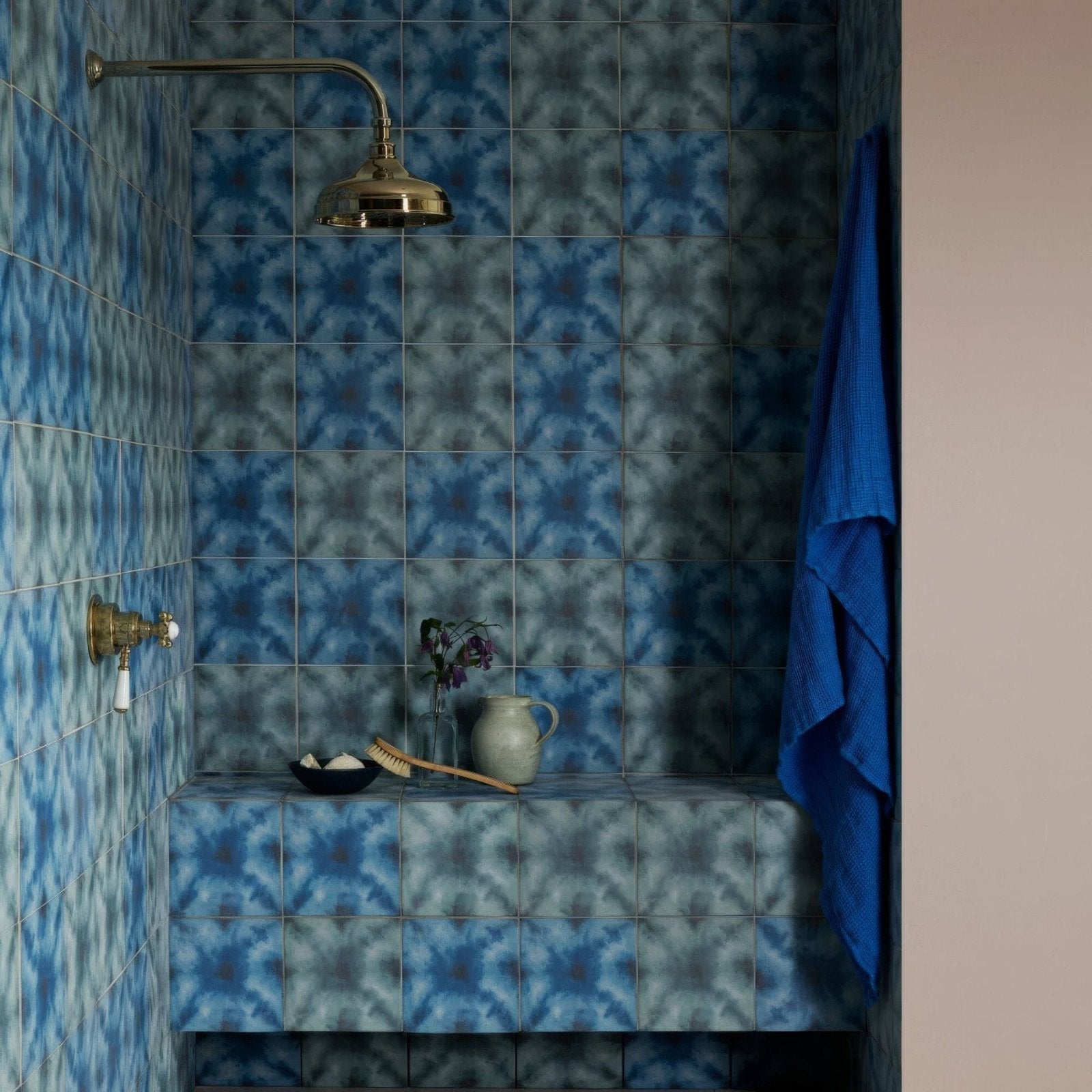 Blue patterned Designers Guild Shibori Cobalt shower tile with brass showerhead and faucet in a bathroom setting