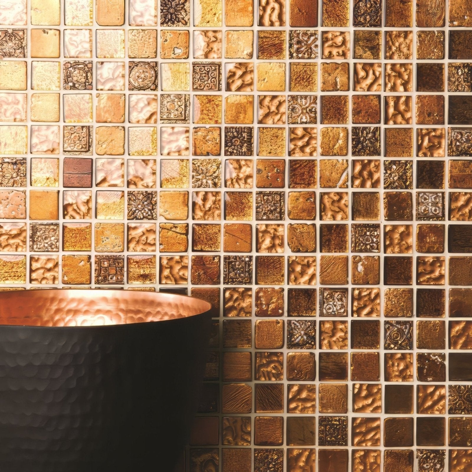 A hammered copper sink with a dark matte finish in front of desire glass and stone mosaic gold and bronze tiles