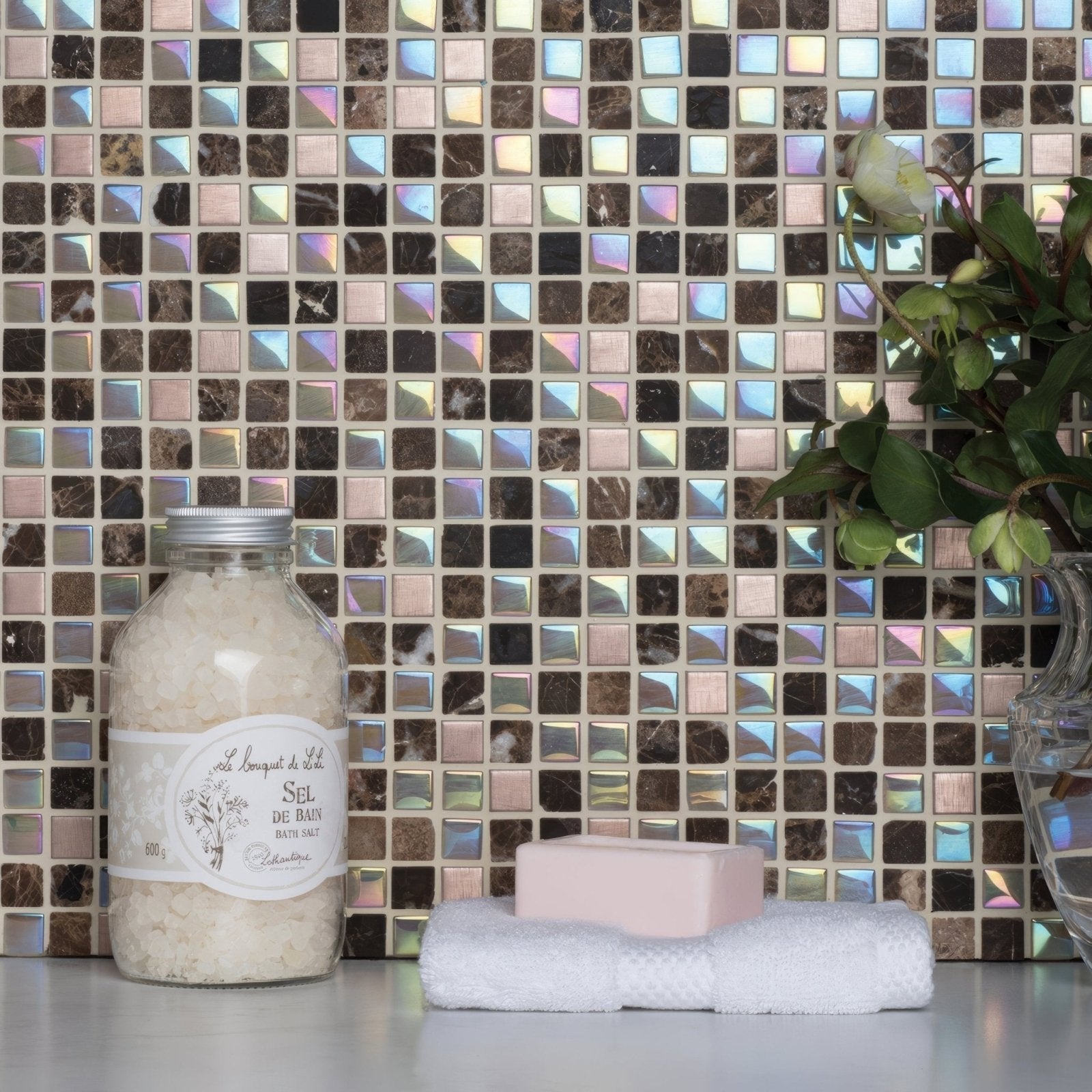 A clear glass jar of white bath salts labeled sel de bain with a silver metal lid from divine earth and fire mixed mosaic