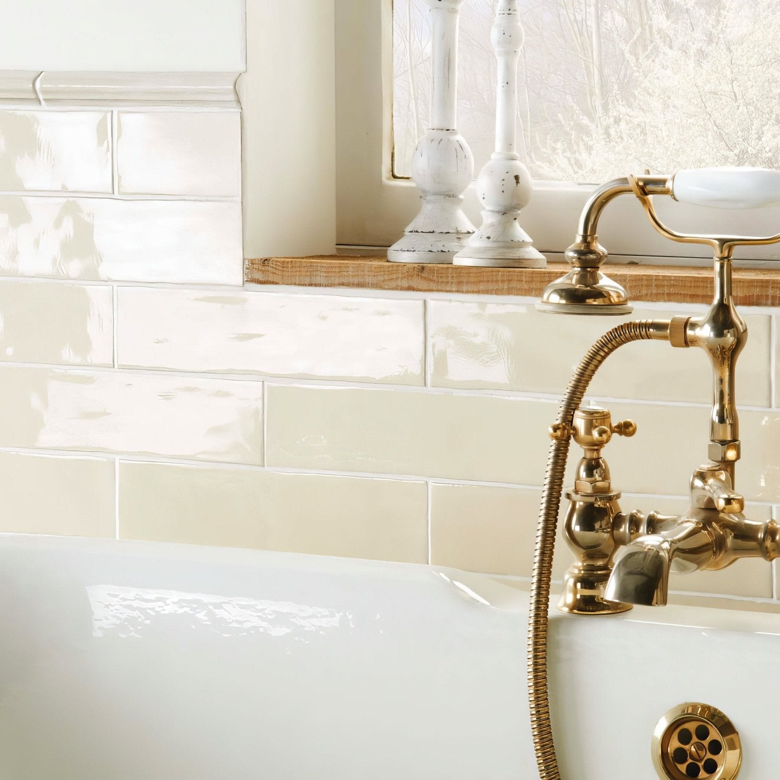 Antique brass bathtub faucet with curved spout and ornate handles against cream large brick tile dune background