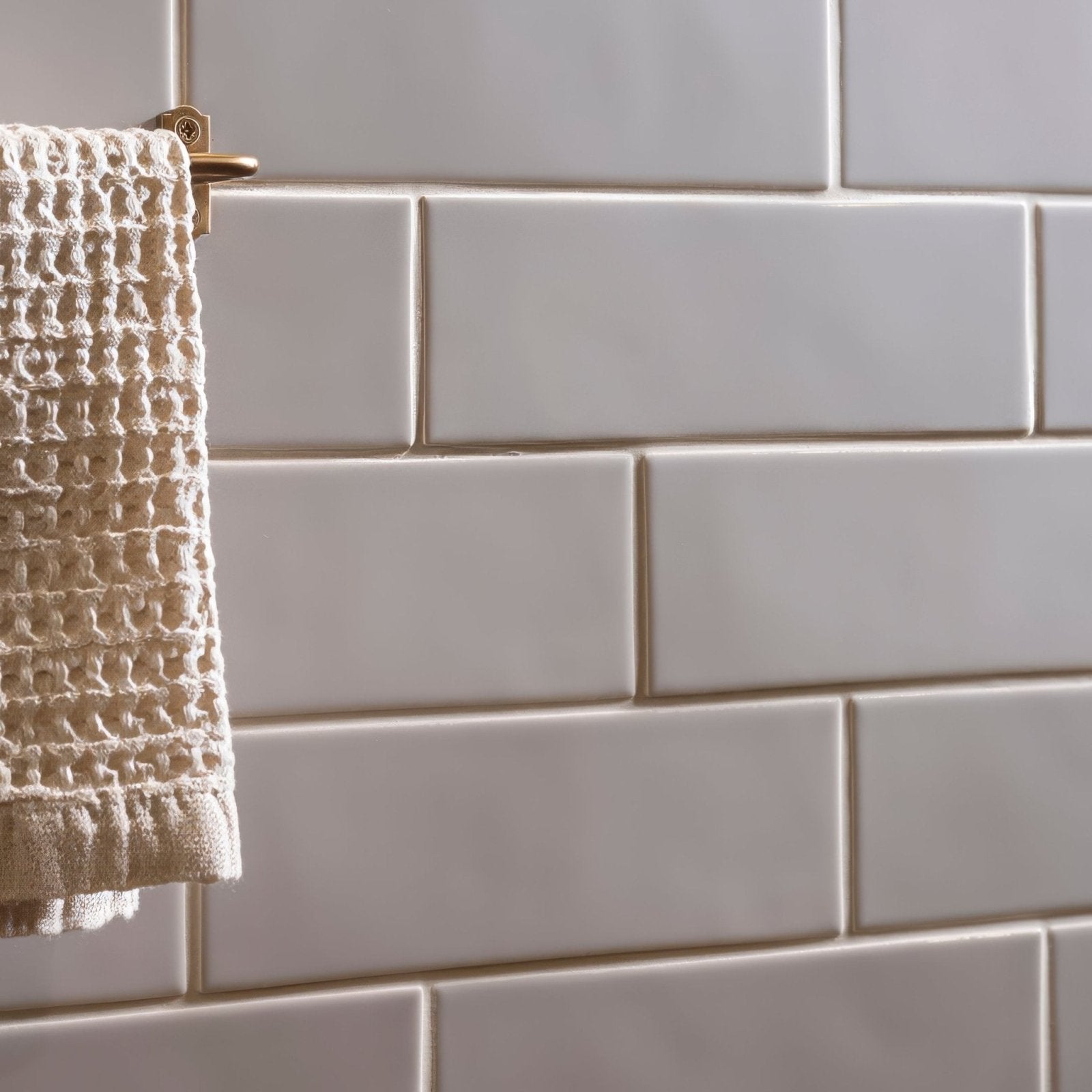 A cream-colored textured waffle-weave towel hanging on a brass rack from the brick tile dunwich collection