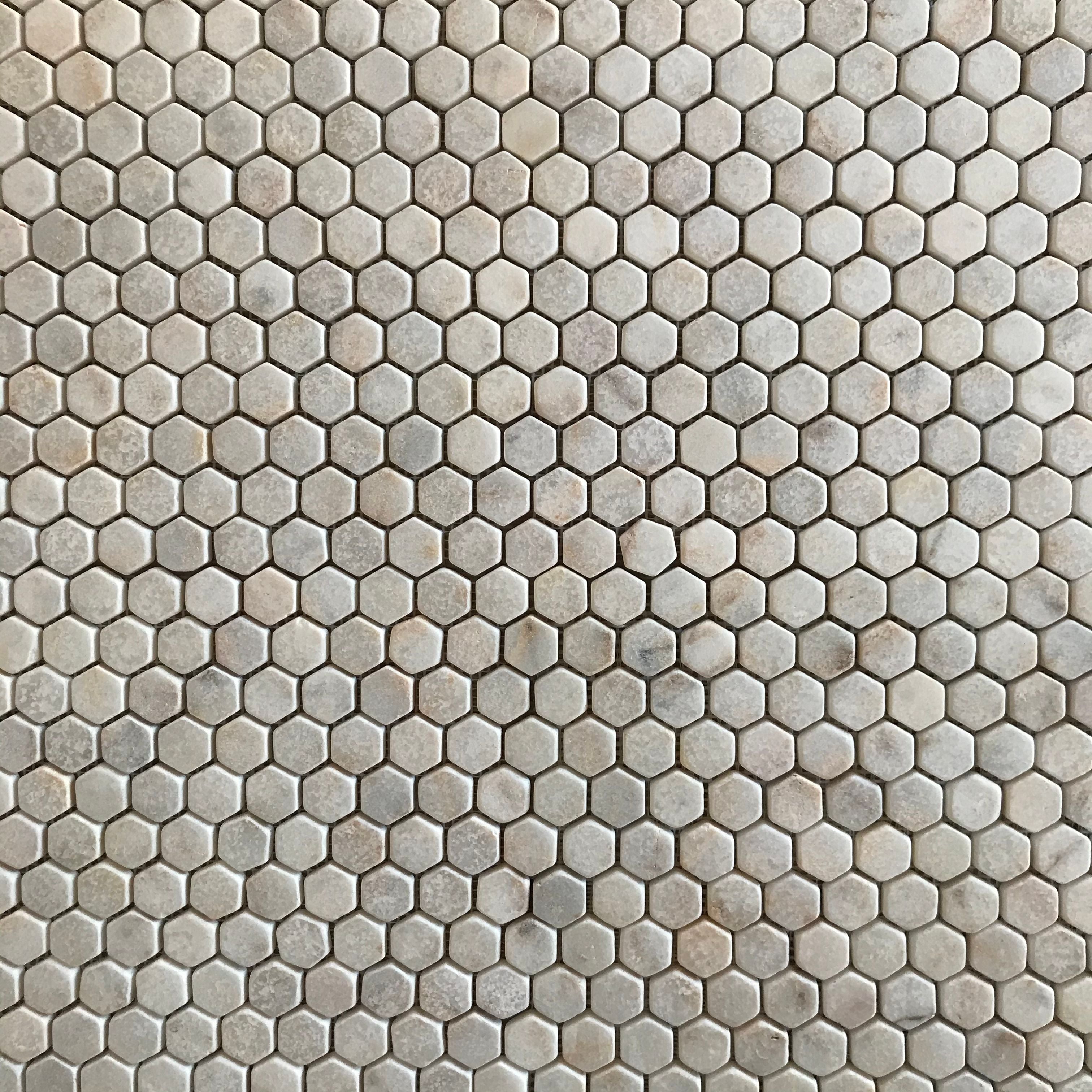 Close view of tumbled Calacatta Sugar hexagons showing worn rounded edges and a lightly pitted matt face