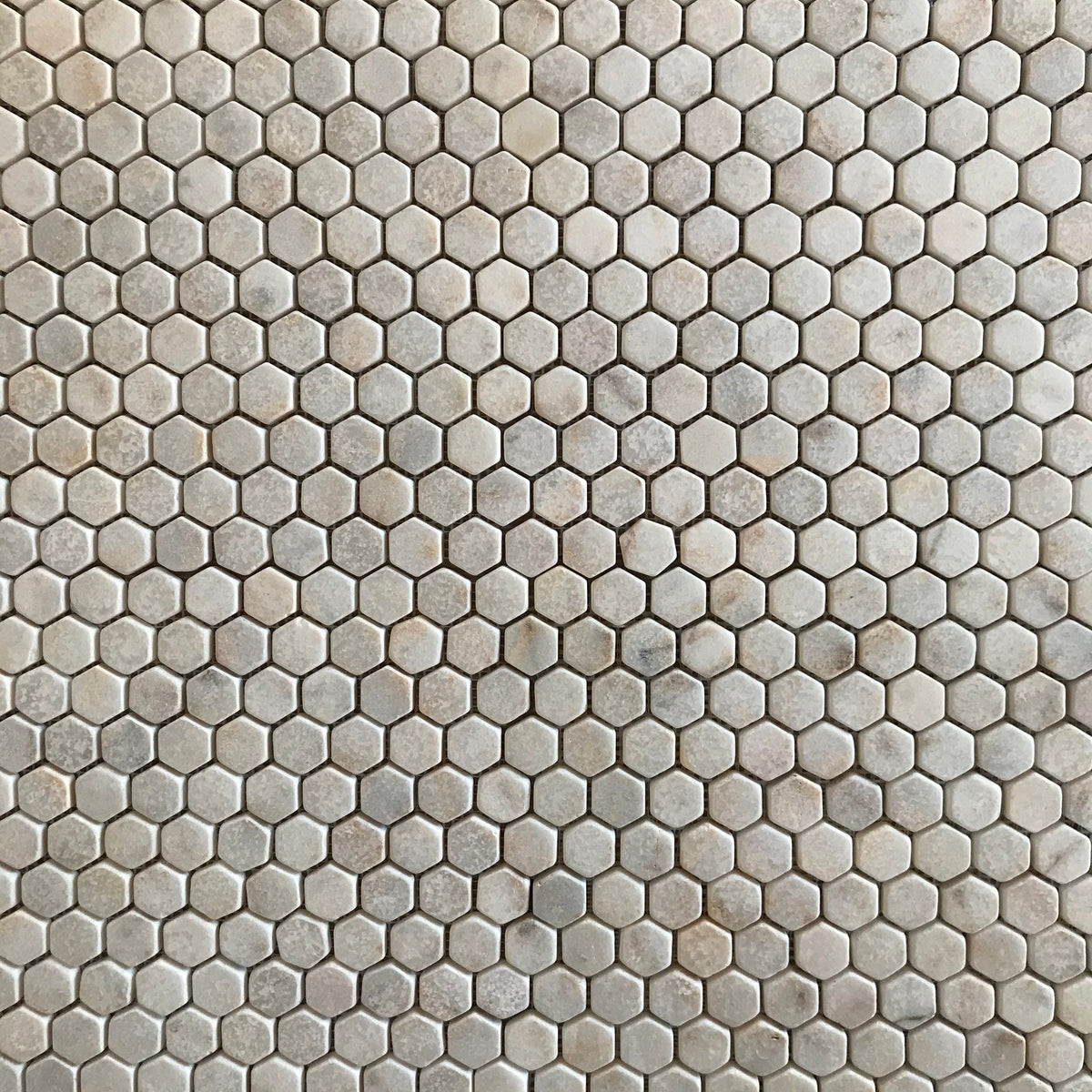 Close view of tumbled Calacatta Sugar hexagons showing worn rounded edges and a lightly pitted matt face
