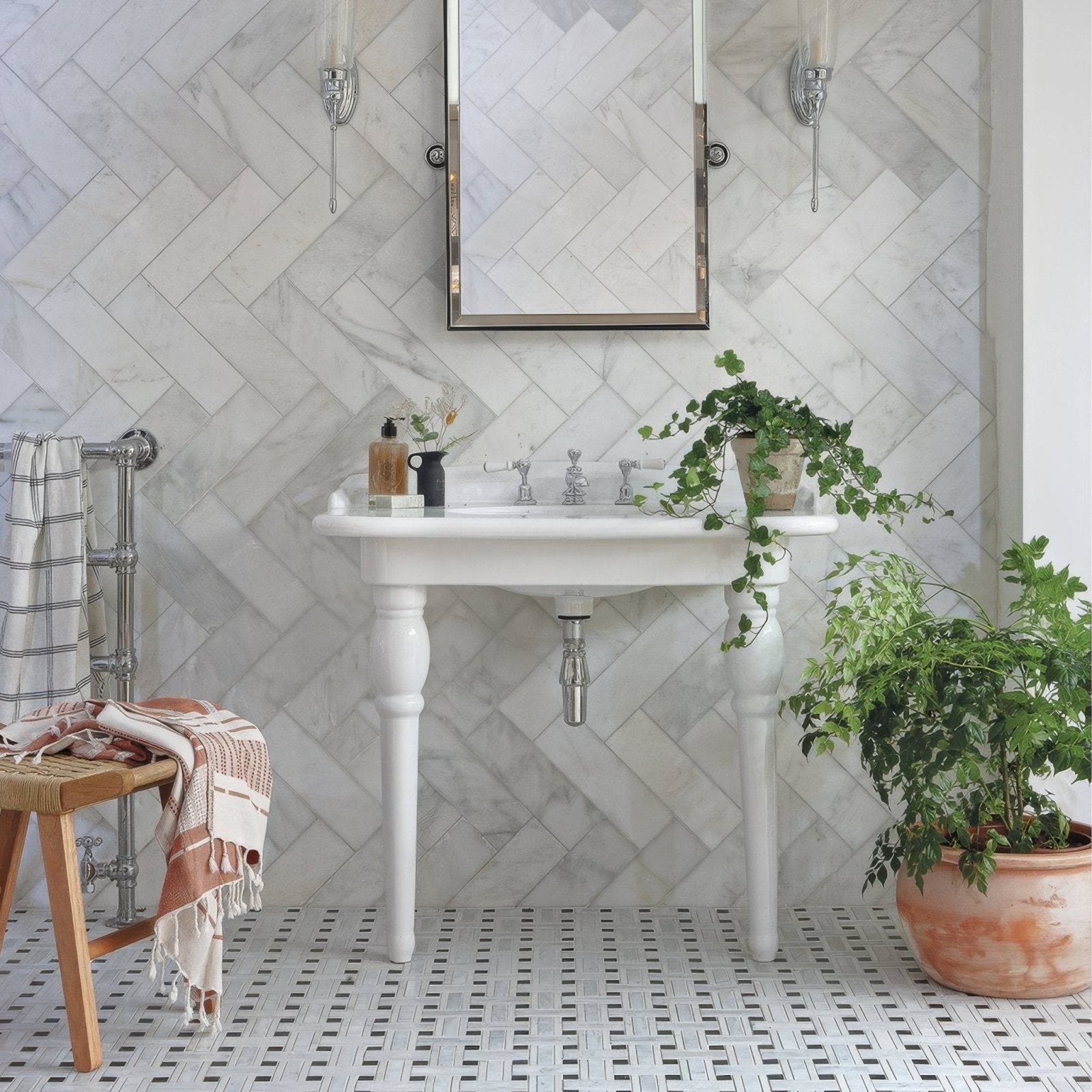 Bathroom with white sink, mirror, and plants against a herringbone-patterned East Hampton Marble Tile 10x30cm wall.