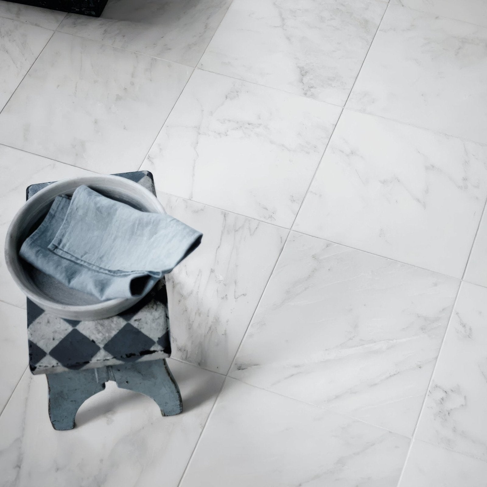 A gray ceramic bowl with a light blue denim garment resting on a black-and-white diamond patterned stool on east hampton marble tile 30x30cm