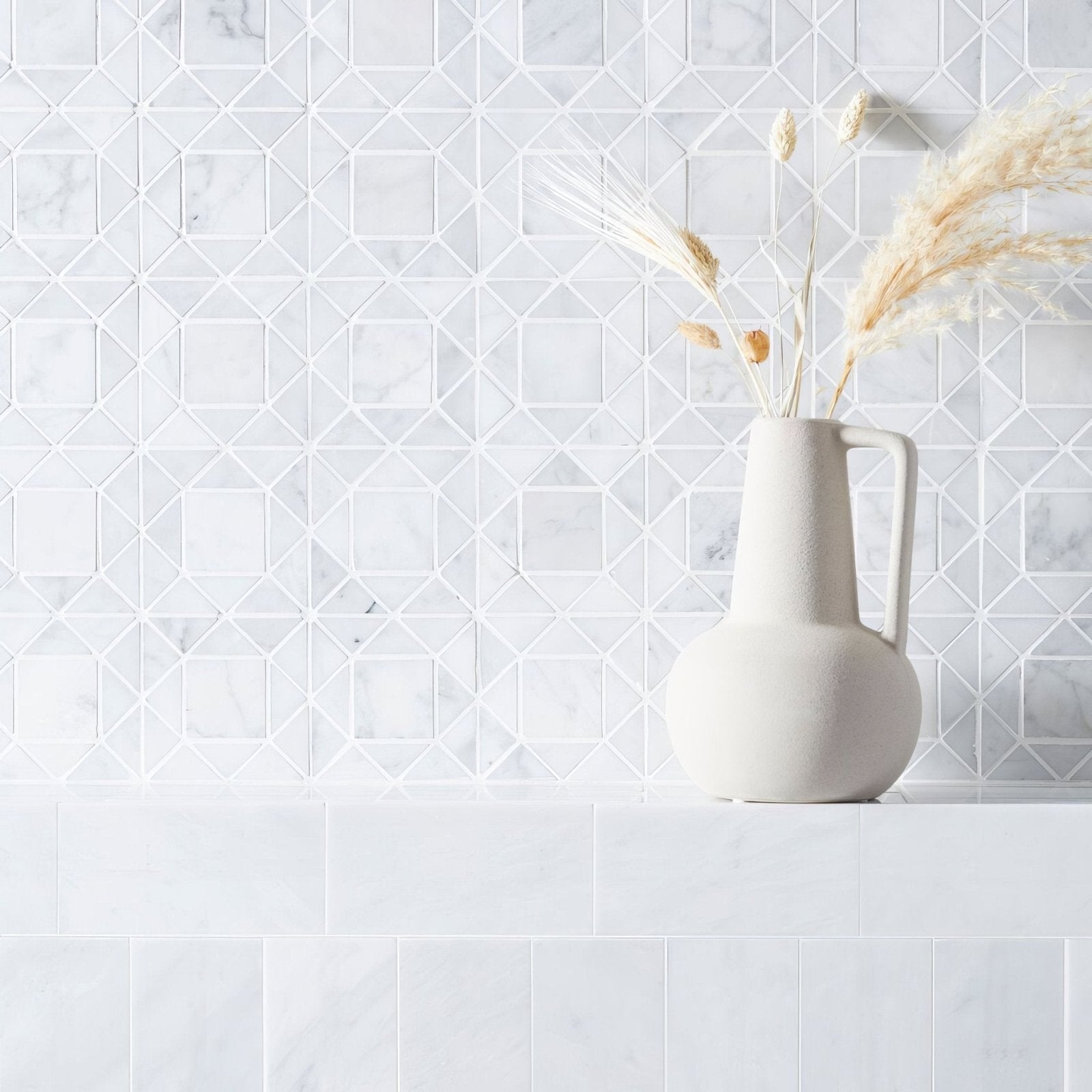 White ceramic pitcher with dried plants against a geometric tile wall in East Hampton Nova Star Marble Mosaic