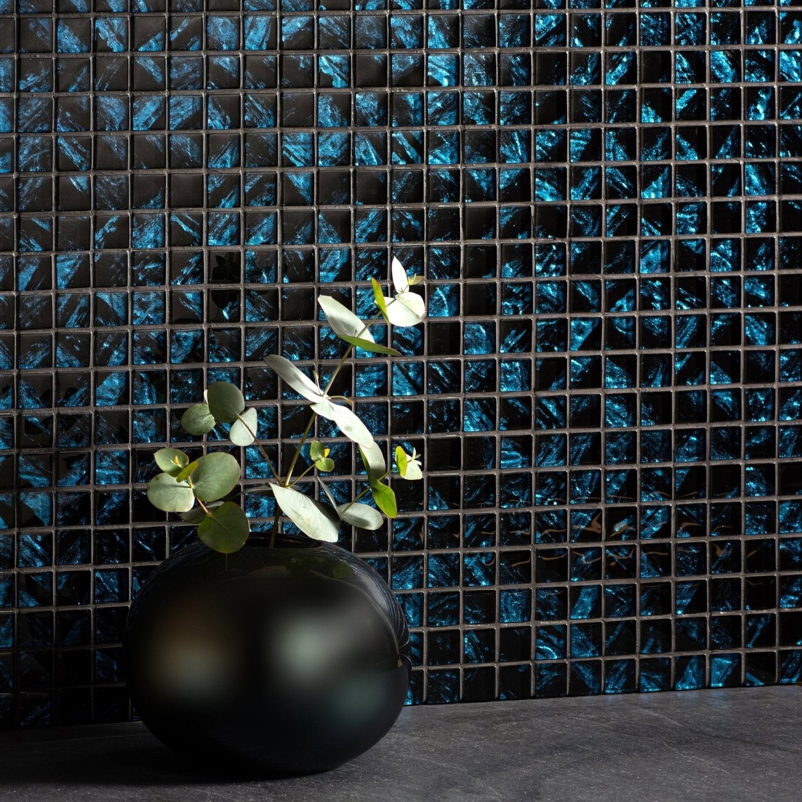 Eden Glass Mosaic blue and black iridescent glass mosaic with a black vase of eucalyptus