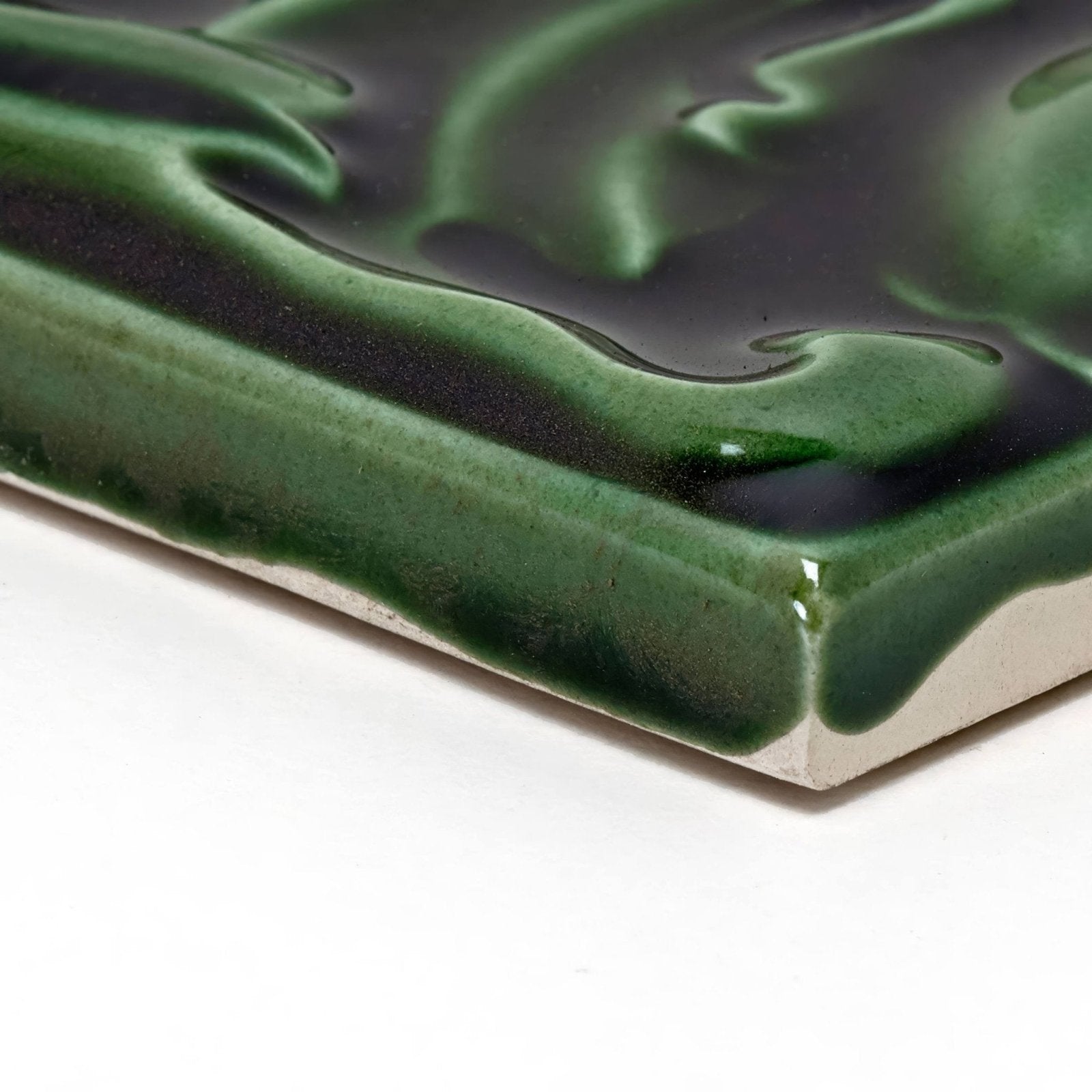 A square ceramic Edwardian Acanthus Caledonian tile with a glossy swirling green glaze over a dark base