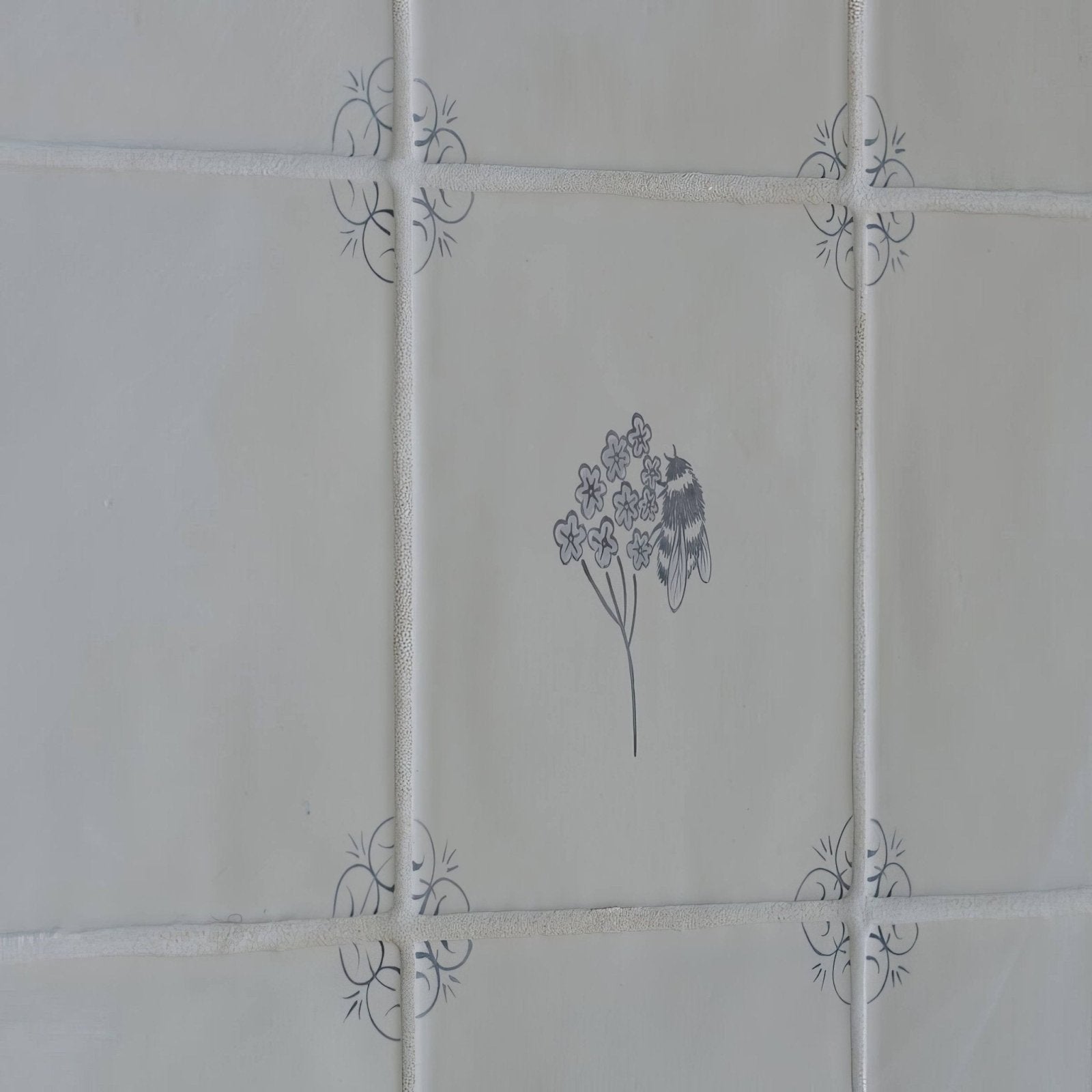 White ceramic tile english delft charcoal bee with gray floral and insect illustration and decorative corner motifs