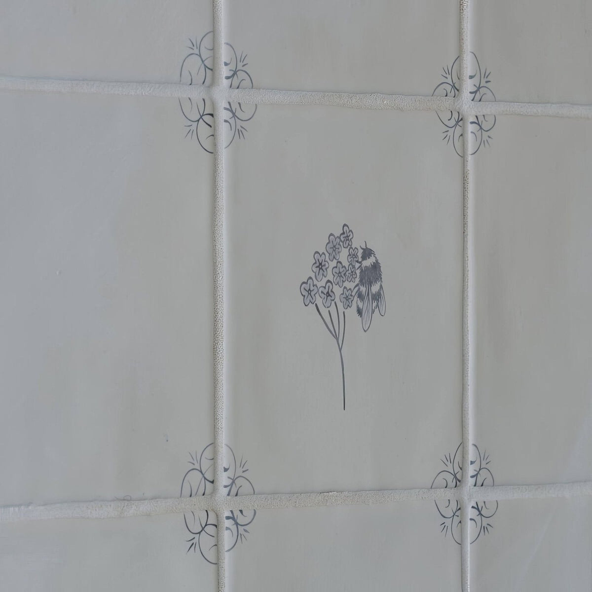 White ceramic tile english delft charcoal bee with gray floral and insect illustration and decorative corner motifs